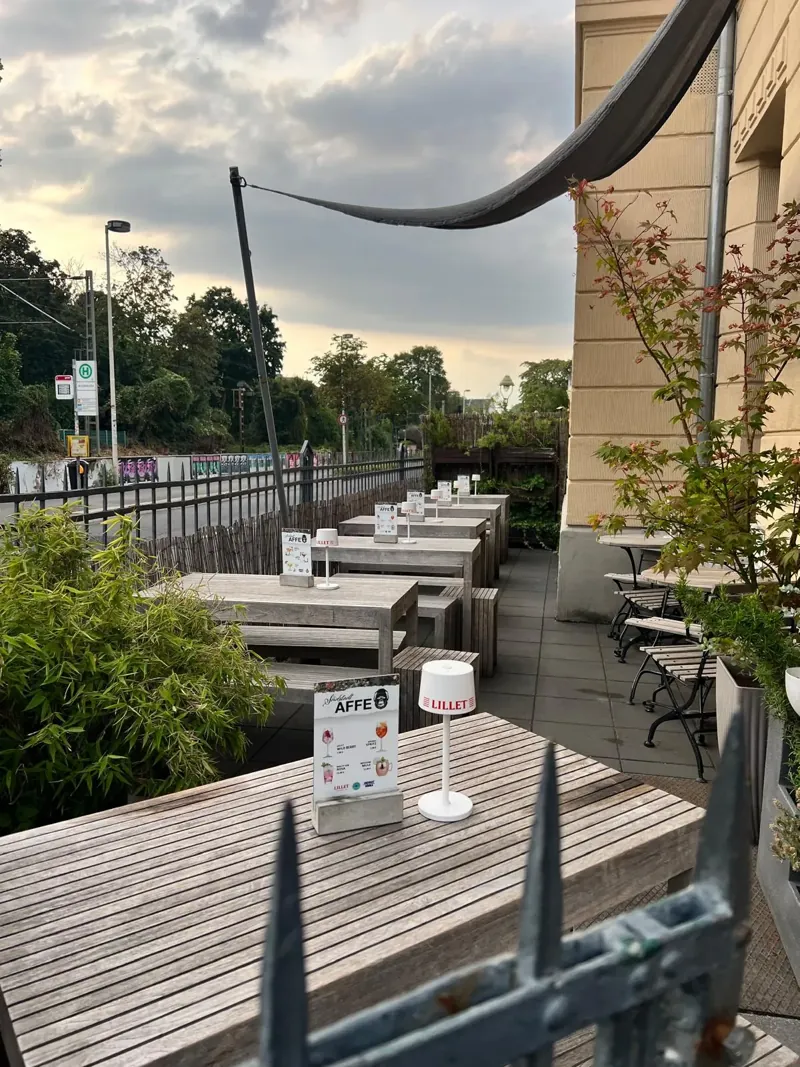 Terrasse der Bar am Abend: Holztische mit Tischlampen, Sonnensegel und Pflanzen